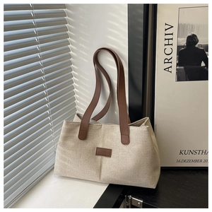 Détail d'un cabas en toile beige avec anses en cuir marron sous une lumière douce