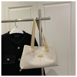 Detail of beige canvas tote bag with brown faux leather straps and minimalist patch