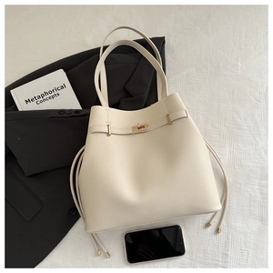 Detail of off-white leather bucket bag with gold twist lock on black blazer backdrop