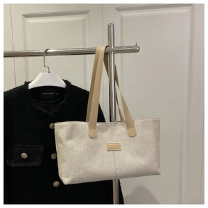 Détail du sac cabas en toile crème avec des anses en cuir marron clair sur un cintre