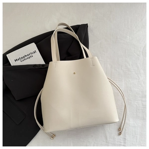 Top view of cream bucket tote bag with gold snap buckle on a black blazer jacket