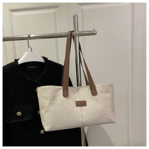 Detail of linen tote bag featuring contrast leather handles and minimalist stitching