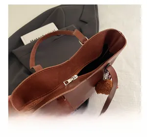 Detailed shot of brown tote bag with smooth silver zipper and plush ball charm accessory