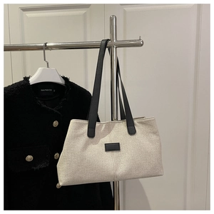 Détail du sac cabas en lin avec anses contrastées noires sur un cintre de vêtements