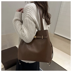 Detail of a large brown matte leather tote bag featuring elegant gold buckles on a model