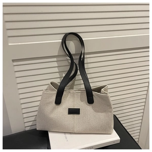 Detail of beige canvas tote with black leather straps and rectangular logo patch