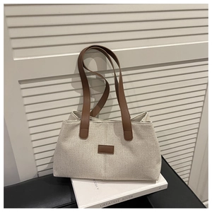 Close-up of beige linen tote bag with brown leather handles and square patch detail