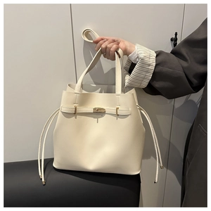 Close-up of cream bucket bag with gold metal buckle held by model in a dark blazer