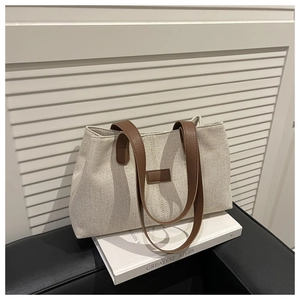 Close-up of textured canvas tote bag with brown leather handles and square logo patch