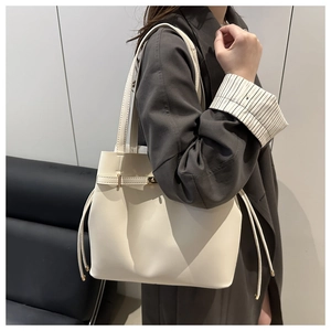 Detail of a large beige faux leather bucket bag with gold buckle strap and side drawstrings