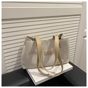 Detail of linen tote bag featuring contrast leather handles and a minimalist patch
