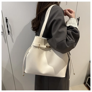 Detail of a minimalist off-white bucket bag with drawstring closure and gold buckle on a coat
