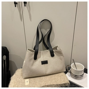 Close-up of a linen tote bag with black leather straps on a cozy beige textured fabric