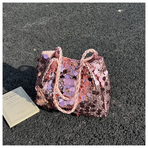 Pink sequin tote bag with woven handles on asphalt road with a fashion book decor