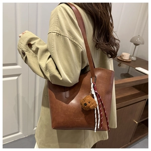 Detail of vintage brown tote bag with leather texture and bear charm on model shoulder