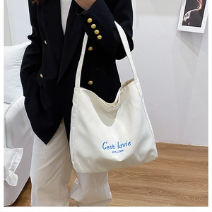Detail of blue 'C'est lavie' embroidery on white canvas large capacity tote bag