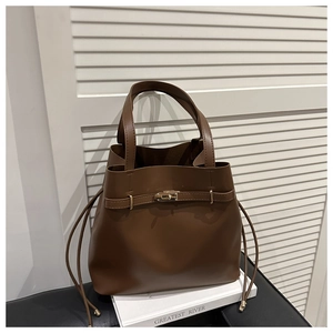 Detailed close-up of brown leather bucket bag with gold metal lock and drawstring detail
