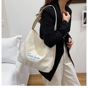 Detail of off-white tote bag with blue C'est la vie embroidery on a female model