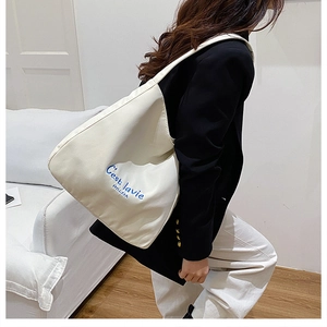 Detail of blue C'est la vie embroidery on off-white canvas tote bag with spacious interior