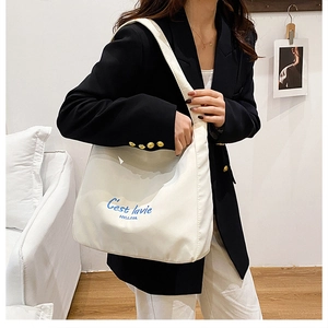 Detail of white canvas tote bag with blue C'est lavie embroidery and premium texture
