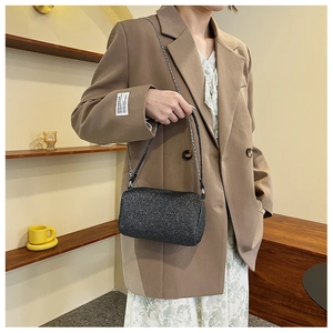Dettaglio borsa a tracolla nera glitterata abbinata a blazer color cammello e catena