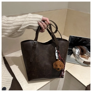 Détail du sac seau en cuir marron foncé avec texture rétro et breloque ours en peluche