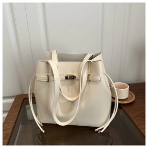 Detail of cream bucket bag showing gold metal clasp and drawstring on wooden table