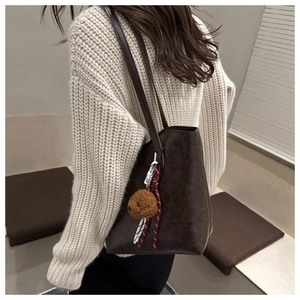 Detail of deep brown tote bag featuring cute teddy bear charm and woven rope decoration