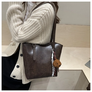Detail of dark brown faux leather tote bag with debossed logo and teddy bear charm