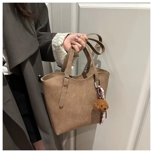Detail of khaki faux leather bucket bag featuring a plush bear charm and branding