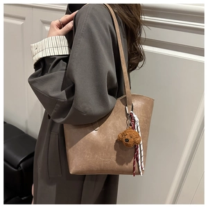 Detailed close-up of khaki tote bag with plush dog charm and long shoulder strap