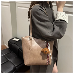 Detail view of light brown tote bag with adjustable strap and plush bear pendant
