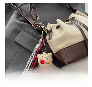 Detail of two-tone bucket bag with braided strap and plush charm on grey fabric