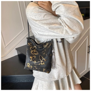 Detalle de bolso de satén negro con bordado de mariposa dorada y borla elegante