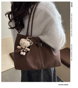 Detail of dark brown faux leather tote bag with a small plush cat charm and white sweater