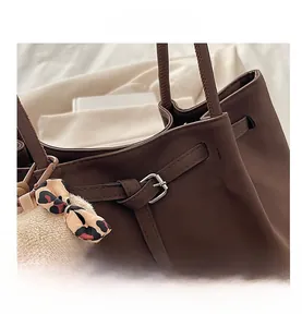 Detail of dark brown matte leather tote bag featuring a decorative belt buckle and plush charm