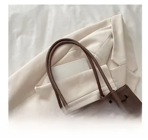 Detail of a large brown matte tote bag with shoulder straps and a leopard print bear charm