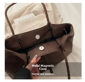Detail view of the magnetic buckle and black lining on a dark brown faux leather tote bag