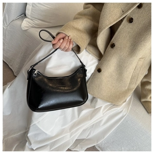 Detail of glossy black patent leather underarm bag with smooth zipper and slim strap
