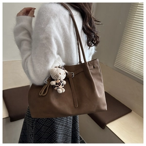 Detail of a brown tote bag with vintage pleats, decorative buckle, and leopard-print charm