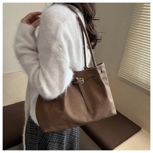 Brown vintage tote bag with buckle details shown on shoulder in minimalist interior