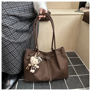 Detail of dark brown leather tote bag featuring a cute plush doll charm on the handle