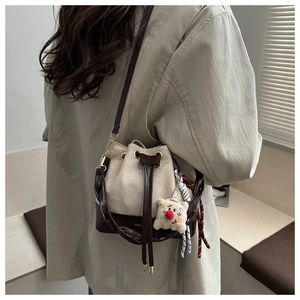 Detail of a beige drawstring bucket bag with brown leather strap and plush charm