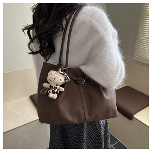 Detail of dark brown matte leather tote bag featuring adjustable buckle and plush charm