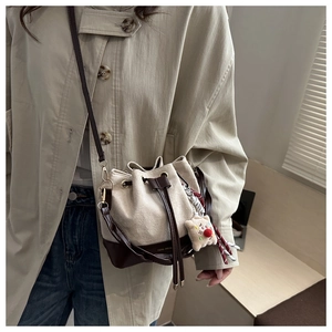 Detail of canvas bucket bag showing leather trim and plush smiley pendant for women