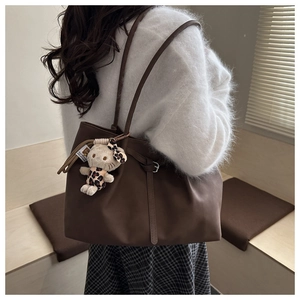 Detail view of large dark brown leather tote bag with a leopard print plush cat charm