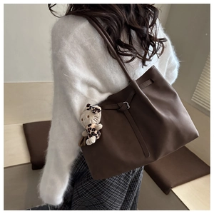 Detail of dark brown leather tote bag featuring slim shoulder straps and a plush charm