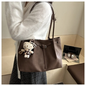 Close-up of large coffee leather tote bag with stylish pleated strap and plush pendant