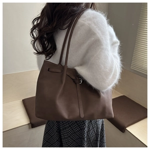 Detail view of a dark coffee leather tote bag featuring side buckles and slim straps