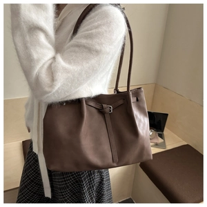 Detail of matte coffee brown leather tote bag with drawstring buckle on a wooden bench